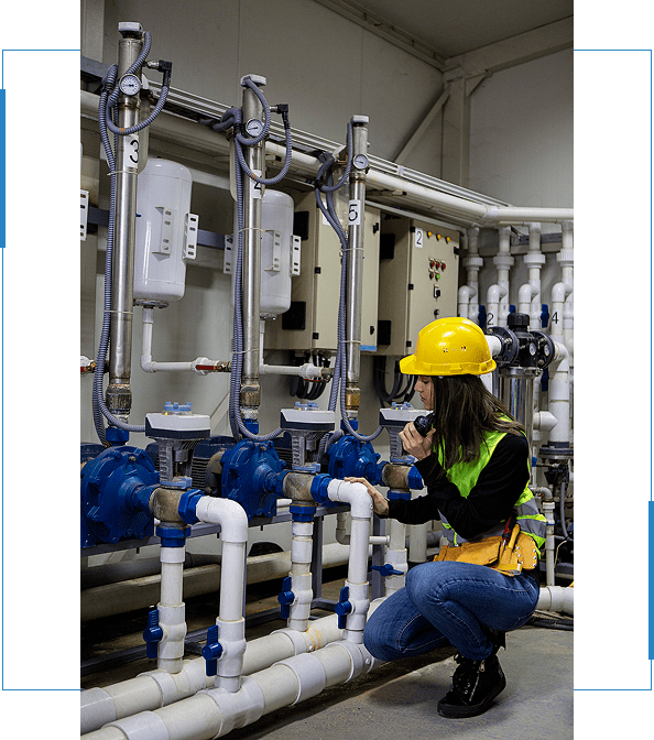 Technician in safety gear inspecting well pump system with blue valves and pipes, emphasizing Pendleton Electric's expertise in water system services.